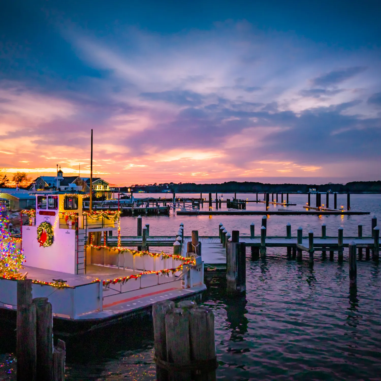 Clouds across a blue and orange sky speckled with clouds above the water where piers can be seen extending from land with the main image a ferry decorated for Christmas.