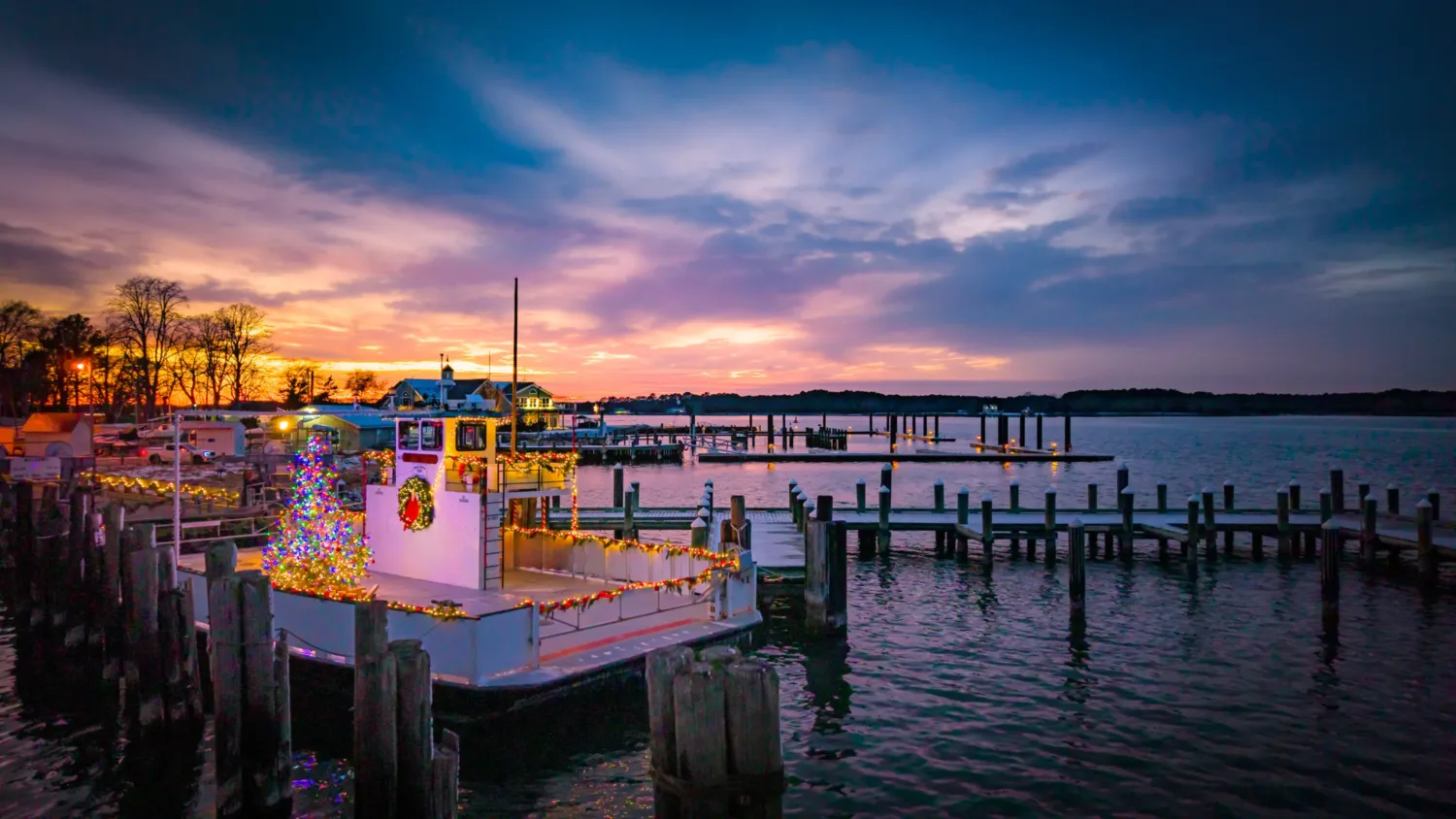Clouds across a blue and orange sky speckled with clouds above the water where piers can be seen extending from land with the main image a ferry decorated for Christmas.