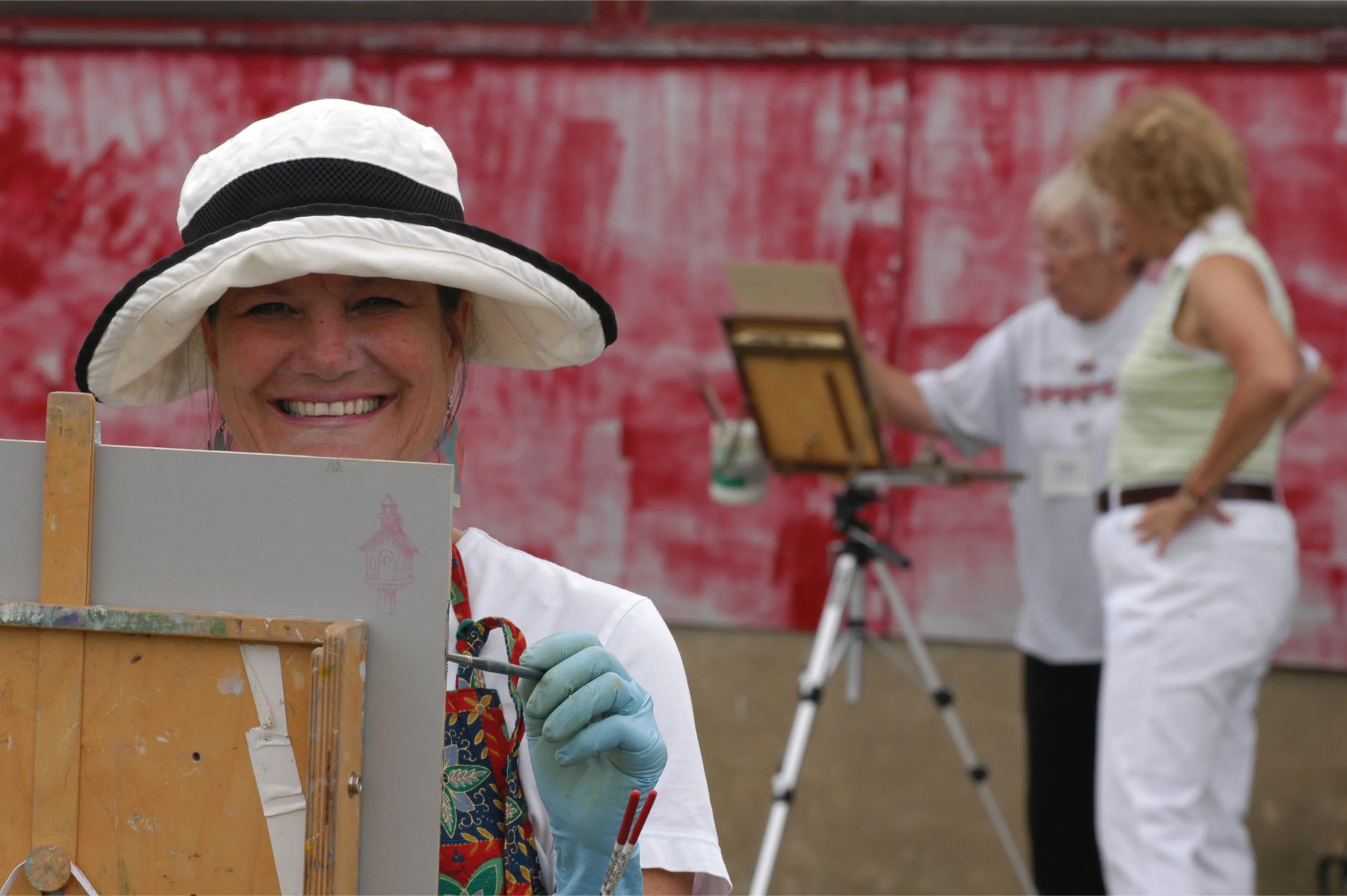 Woman wearing hat smiling, while painting in Plein Air.