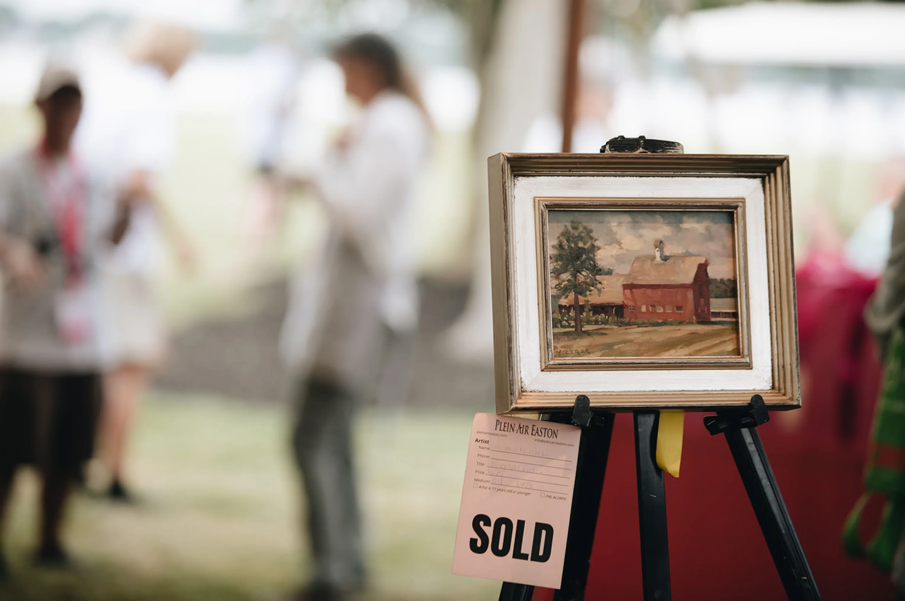 Small painting of a red barn with a Sold tag hanging from it.