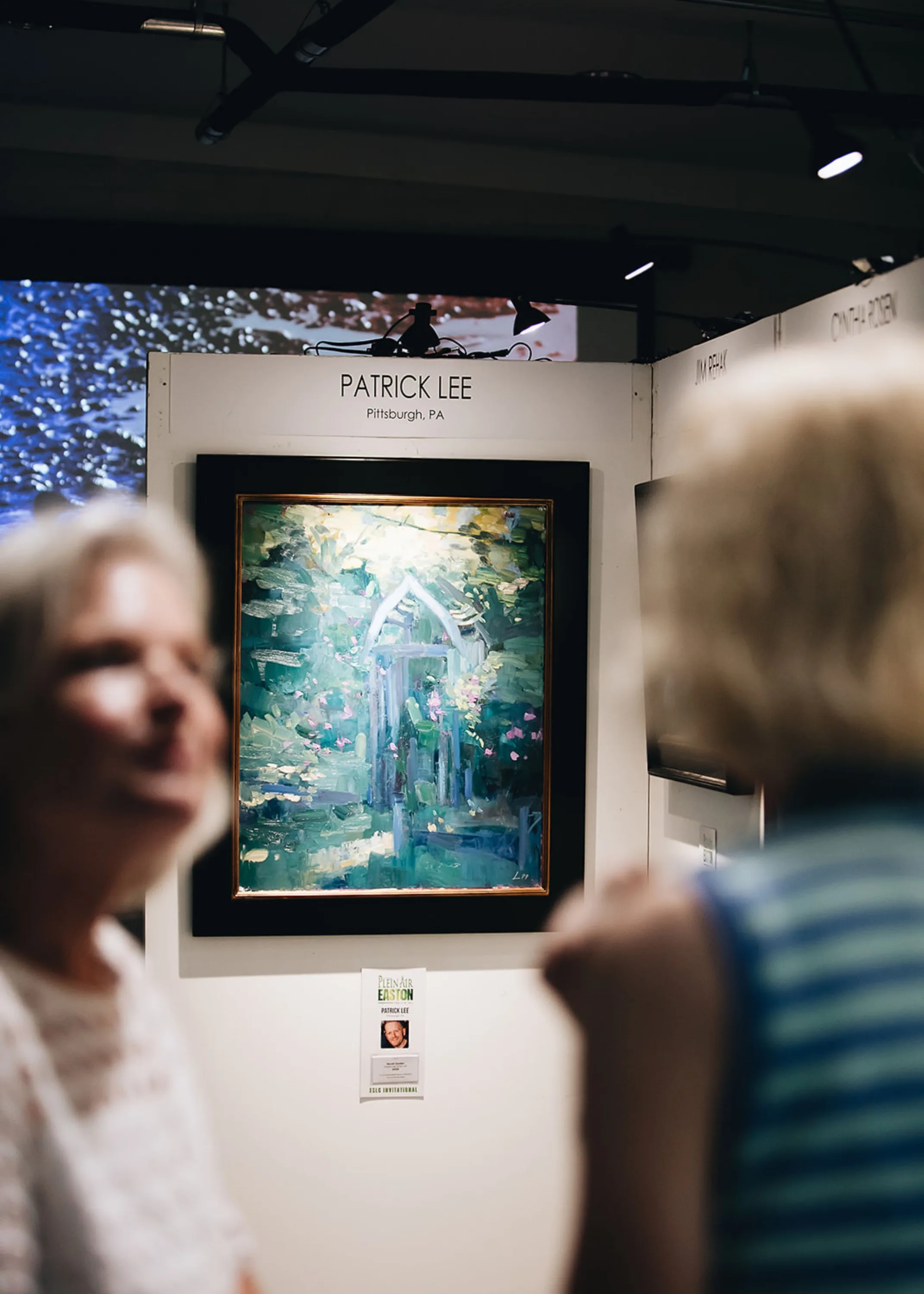 Patrick Lee painting hanging in the background while two women speak in front of it.