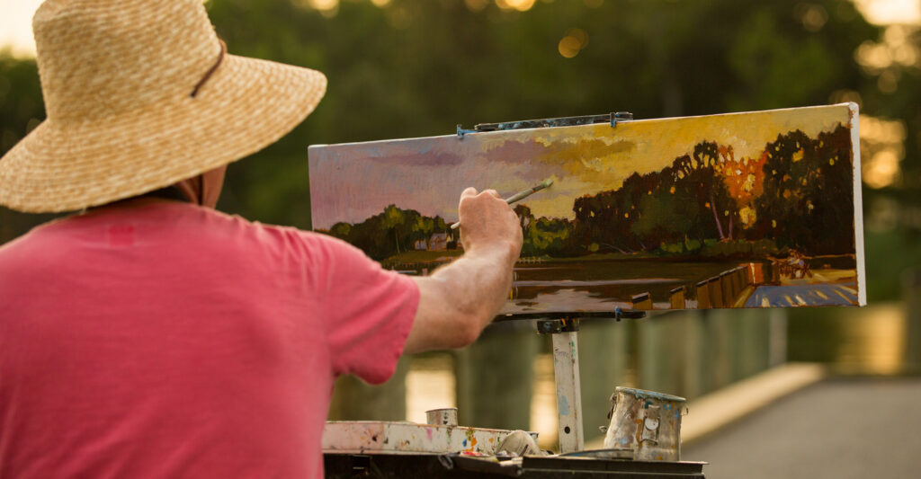 Artist with back to camera painting in plein air.