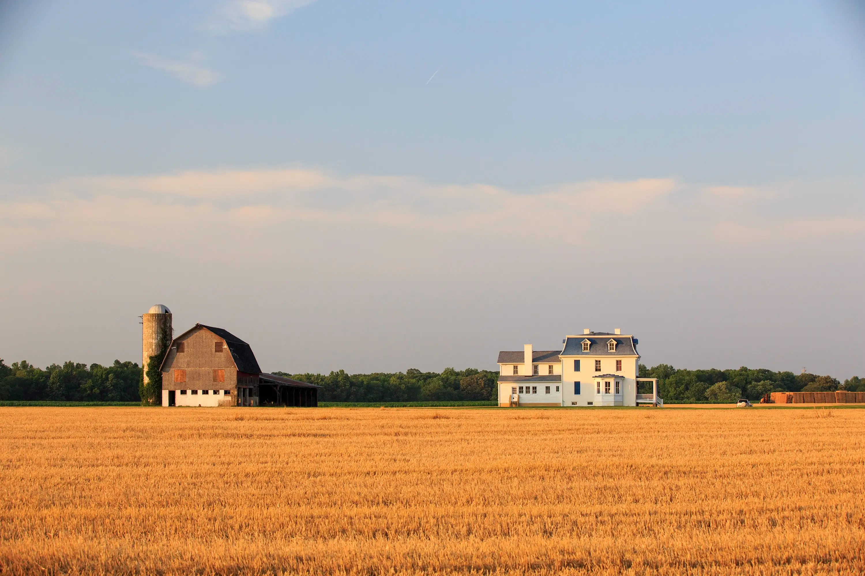 A farmhouse and barn in behind a field.
