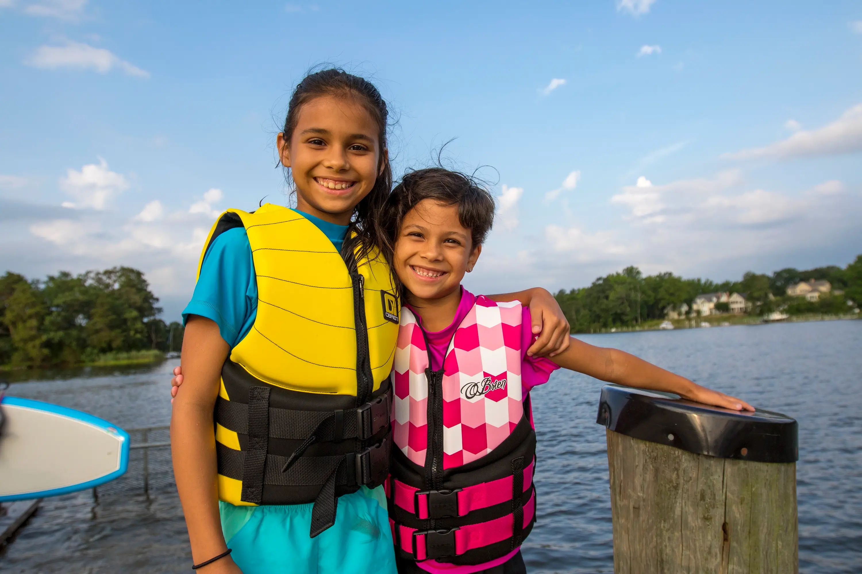 Kid wearing life jackets smiling on the dock.