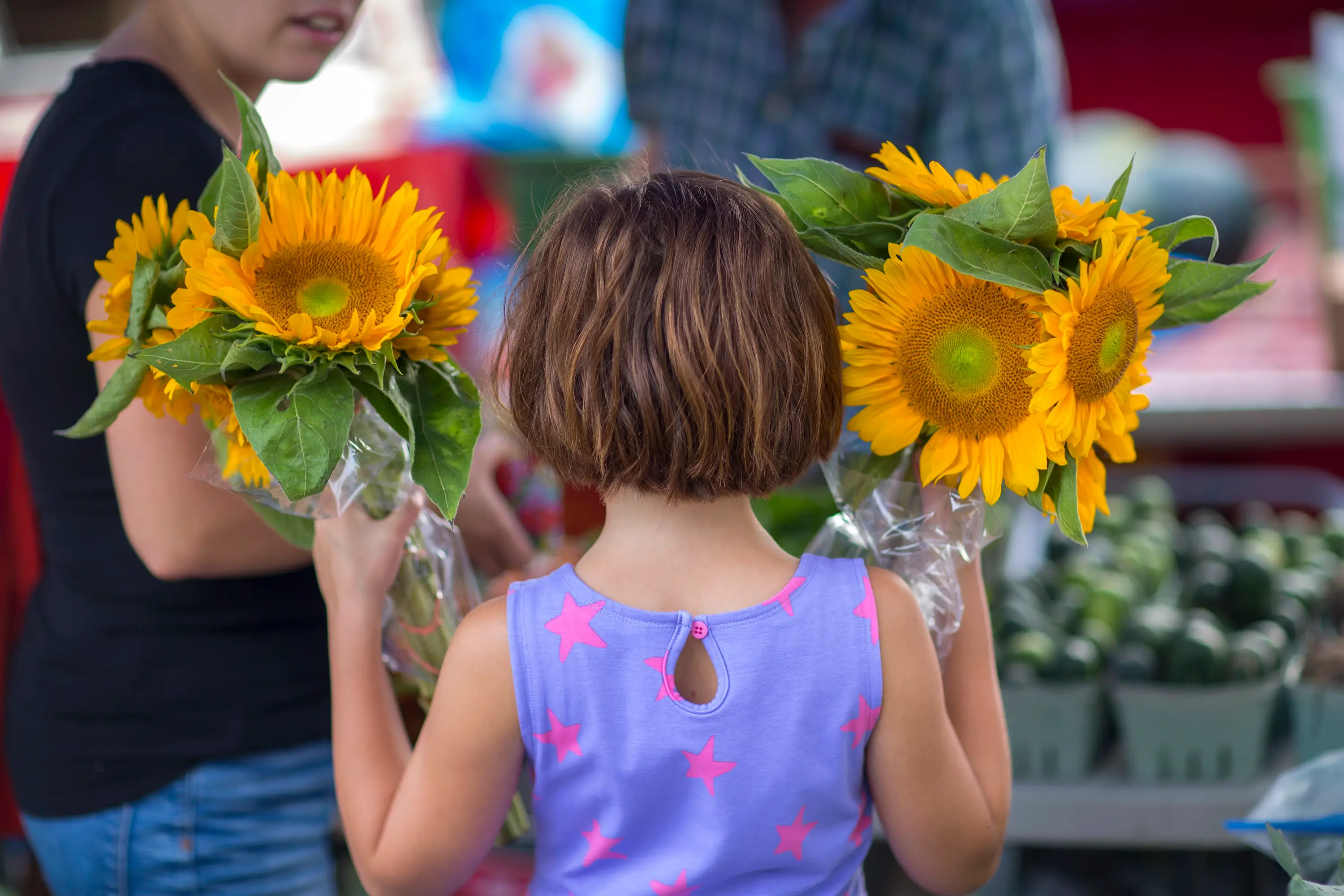 A girl with sunflowers in hand at the Farmers Market.